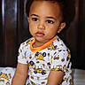 toddler, child, pajamas, construction_theme, sitting, indoor, portrait, cute, young_child, curly_hair, face, expression, clothing, bed, furniture, person, skin, eyes, lips, home