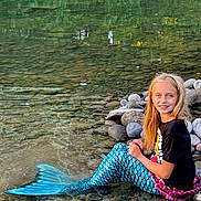 Ariana joined the competition — help win amazing prizes! child, girl, mermaid_tail, water, river, rocks, smile, long_hair, nature, outdoor, reflection, blue, black_tshirt, playful, sitting, shallow_water, daylight, scenery, casual_clothing, happy