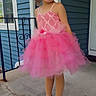 Gianna is registered to the contest to win money with this photo: child, girl, pink_dress, tutu, crocs, bow, curly_hair, smiling, porch, concrete, railing, house, window, door, outdoor, happy, fashion, footwear, pose, playful