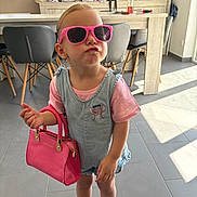 Maëlya participe au concours pour gagner de l'argent avec cette photo : attitude, chairs, child, cute, denim_overall, fashion, floor_tiles, handbag, indoor, kitchen, modern, person, pink_shirt, pink_sunglasses, playful, pout, sneakers, sunlight, table, toddler