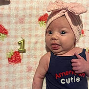 Paisley joined the competition — help win amazing prizes! baby, infant, cute, headband, bow, tongue_out, birthday_candle, number_one, blanket, strawberry_pattern, blue_tank_top, text_on_clothing, lying_down, playful, portrait, child, skin, face, expression, celebration