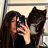 Yumi participe au concours pour gagner de l'argent avec cette photo : woman, dog, pet, mirror_selfie, portrait, long_hair, brown_hair, blue_eyes, fluffy, collar, indoors, window, reflection, smartphone, phone_case, black_clothing, jewelry, sitting, cute, photography
