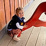 child, toddler, smiling, wooden_wall, wooden_floor, red_bench, bench, blue_eyes, sweater, dress, hands, shoes, sitting, portrait, planks, outdoors, wood_paneling, cute, light, young_child