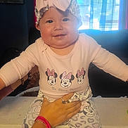Genesis is registered to the contest to win money with this photo: baby, child, infant, smiling, portrait, indoors, window, backlighting, bow, headband, minnie_mouse, disney, clothing, long_sleeves, patterned_pants, sitting, adult_hand, support, happy, family