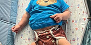 Oliver is registered to the contest to win money with this photo: baby, infant, child, playpen, blue_shirt, monkey_graphic, diaper, patterned_diaper, hot_air_balloon_pattern, mattress, lying_down, barefoot, cute, curious, indoor, soft_lighting, plush, baby_clothing, person, face