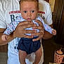 baby, infant, person, hands, clothing, indoor, blue_eyes, shorts, long_sleeve, tshirt, adult, carpet, door, furniture, cup, table, curious, holding, portrait, closeup