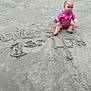 baby, child, beach, sand, swimsuit, pink, sitting, portrait, outdoor, footprints, writing, celebration, first_birthday, serious_expression, water, summer, vacation, nature, person, fun
