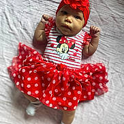 Naomi is registered to the contest to win money with this photo: accessories, baby, bonnet, cap, clothing, costume, doll, dress, face, formalwear, hat, head, headband, newborn, pattern, person, photography, portrait, sitting, toy