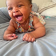 Jamila is registered to the contest to win money with this photo: baby, smiling, happy, infant, bed, pillow, blanket, indoors, child, person, cute, clothing, floral, skin, face, hands, lying_down, expression, joy, toddler