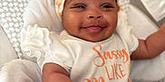 Jamila is registered to the contest to win money with this photo: baby, smiling, headband, infant, baby_seat, cushion, white_clothing, orange_text, happy, indoor, child, cute, person, portrait, soft_toys, seatbelt, baby_girl, patterned_fabric, closeup, comfortable