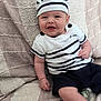 baby, infant, smiling, hat, striped_clothing, sitting, blanket, cute, happy, child, portrait, indoor, young, person, casual_clothing, comfortable, funny_hat, cozy, small_person, cheerful