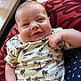 baby, smiling, infant, clothing, palm_tree_pattern, cushion, hand, indoor, cute, face, chubby_cheeks, onesie, relaxed, person, portrait, skin, happy, closeup, child, comfort