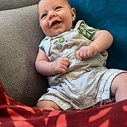 Lyam participe au concours pour gagner de l'argent avec cette photo : baby, smiling, infant, couch, blue_cushion, clothing, overalls, green_shirt, happy, face, human, indoor, portrait, seated, red_fabric, cozy, cute, child, skin, relaxed