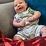 baby, smiling, infant, couch, blue_cushion, clothing, overalls, green_shirt, happy, face, human, indoor, portrait, seated, red_fabric, cozy, cute, child, skin, relaxed