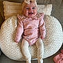 apparel, baby, bow, child, cozy, cushion, cute, happy, headband, indoor, infant, knitted, patterned_cushion, pink_clothing, portrait, seated, smiling, sofa, tights, young_child