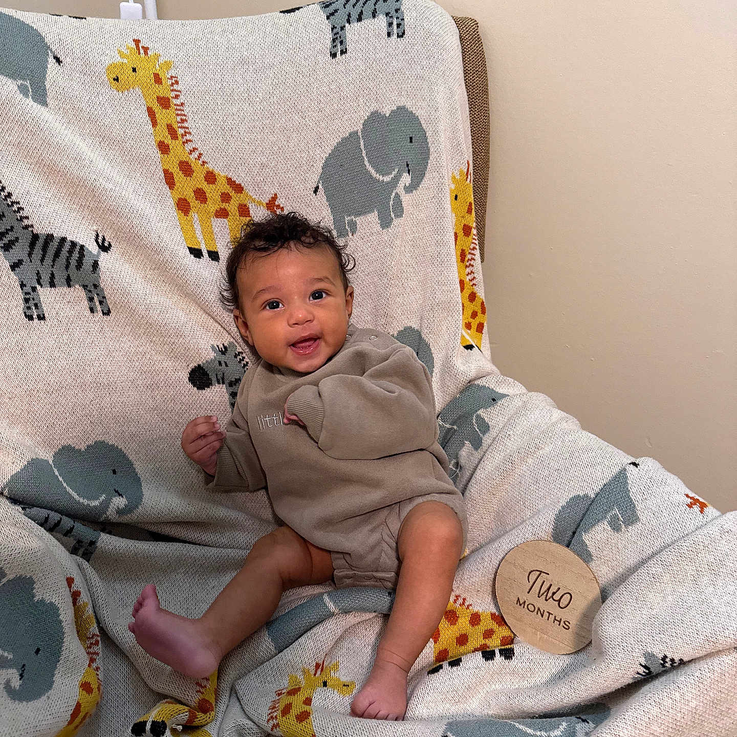 Dakotah joined the competition — help win amazing prizes! animal_print, baby, blanket, child, clothing, cozy, cute, elephant, giraffe, happy, indoors, infant, neutral_wall, portrait, sitting, smiling, soft_lighting, two_months, wooden_sign, young_child