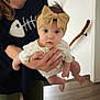 baby, child, headband, bow, adult_hand, person, indoor, floor, wooden_floor, white_wall, handrail, long_sleeve, curious, wide_eyes, holding, clothing, black_shirt, fishbone_design, human, portrait