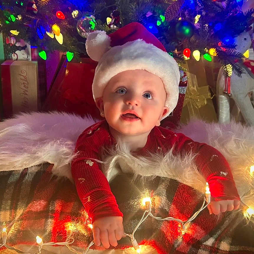 Jack is registered to the contest to win money with this photo: baby, blanket, celebration, child, christmas, christmas_tree, cozy, cute, decorations, festive, gift_boxes, holiday, holiday_lights, indoor, infant, plush, red_clothing, santa_hat, smiling, winter