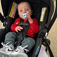 Jack is registered to the contest to win money with this photo: baby, pacifier, car_seat, sneakers, red_sweater, green_pants, child, infant, seatbelt, footwear, person, outdoor, curious, wide_eyes, black_car_seat, clothing, cute, sitting, safety, infant_boy