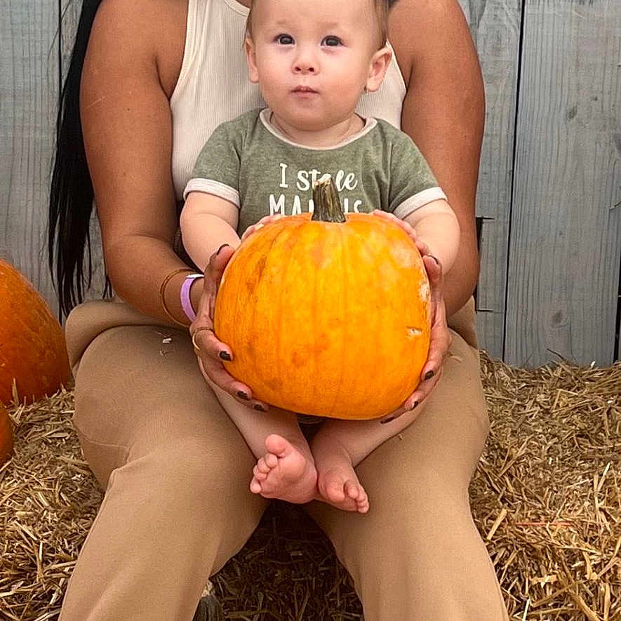 Julius joined the competition — help win amazing prizes! woman, baby, pumpkin, hay, autumn, smile, outdoor, fall, clothing, sneakers, wooden_fence, person, child, nature, seasonal, portrait, holding, sitting, happy, family