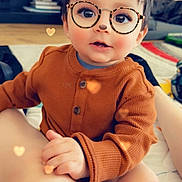 Aiden is registered to the contest to win money with this photo: child, toddler, indoors, brown_sweater, glasses_filter, bear_ears_filter, heart_bokeh, cute, sitting, face, hand, legs, floor, carpet, furniture, playful, digital_filter, portrait, smile, cozy