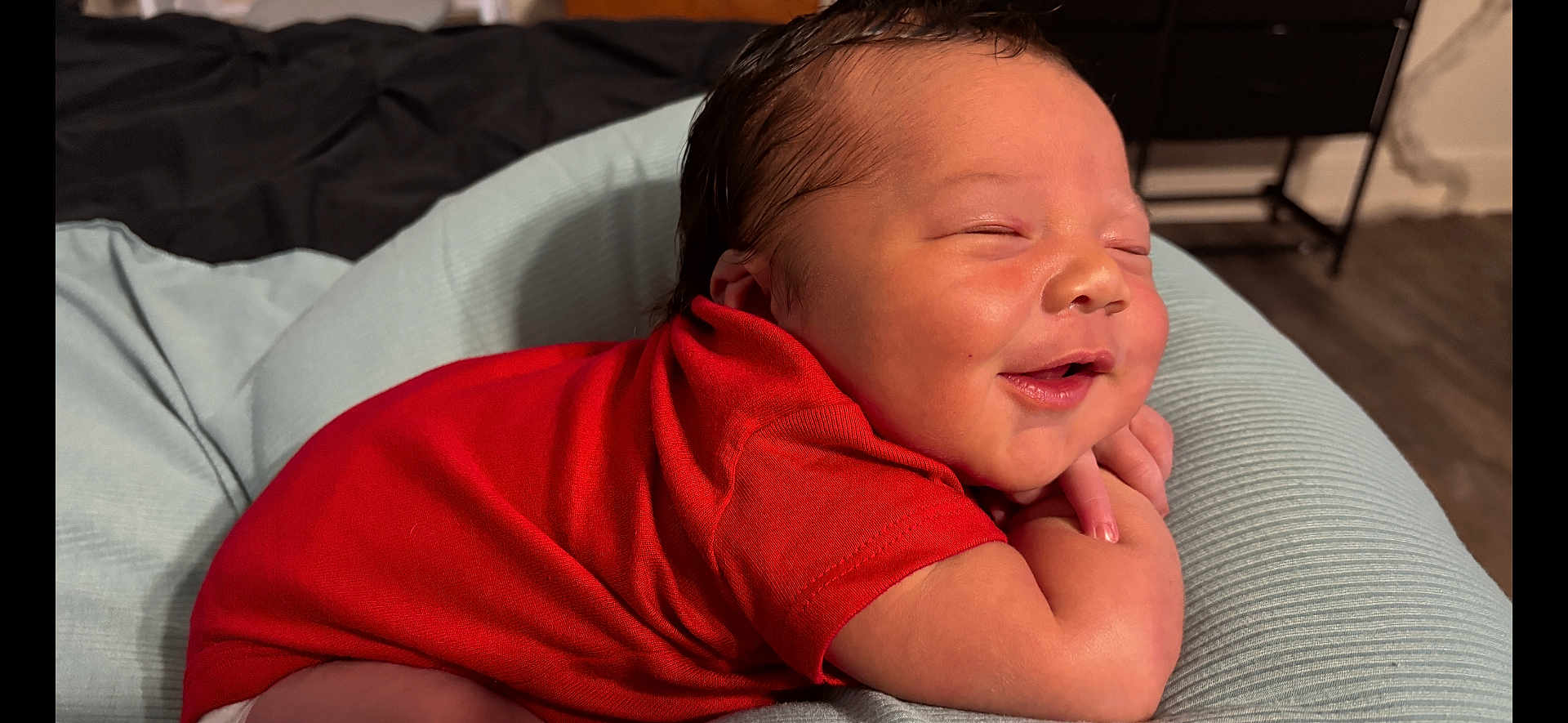 Asaiah joined the competition — help win amazing prizes! baby, newborn, smiling, red_clothing, cushion, resting, indoors, happy, infant, cute, sleeping, face, skin, child, person, soft, comfort, home, portrait, toddler