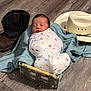 Asaiah joined the competition — help win amazing prizes! baby, newborn, swaddle, basket, blanket, floor, wooden_floor, cowboy_boot, cowboy_hat, hat, footwear, sleeping, infant, person, indoors, portrait, cute, resting, dinosaur_pattern, wrapped