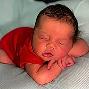 Asaiah is registered to the contest to win money with this photo: baby, newborn, sleeping, red_onesie, cushion, soft_texture, peaceful, infant, closeup, resting, cute, child, portrait, indoor, skin, head, hands, closed_eyes, adorable, small