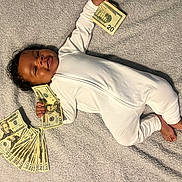 Santana joined the competition — help win amazing prizes! baby, infant, money, twenty_dollar_bills, onesie, blanket, smiling, lying_down, hand, foot, currency, cash, cute, indoors, child, person, happy, small, finance, rich