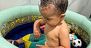Jacob is registered to the contest to win money with this photo: toddler, child, inflatable_pool, water, toy, cup, bathroom, wet_hair, banana_pattern, indoor, playing, summer, fun, cute, swimming_pool, plastic_toys, soccer_ball_toy, football_toy, skin, small