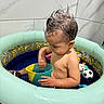 toddler, child, inflatable_pool, water, toy, cup, bathroom, wet_hair, banana_pattern, indoor, playing, summer, fun, cute, swimming_pool, plastic_toys, soccer_ball_toy, football_toy, skin, small