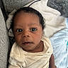 Dallas is registered to the contest to win money with this photo: baby, infant, child, face, eyes, curly_hair, onesie, blanket, couch, soft_texture, indoors, portrait, closeup, cute, young, skin, small_hand, seated, looking_up, comfortable