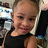 black_clothing, casual, child, closeup, curly_hair, cute, earrings, face, furniture, hair_puff, happy, home, indoor, living_room, person, portrait, smiling, television, tutu_dress, young_child