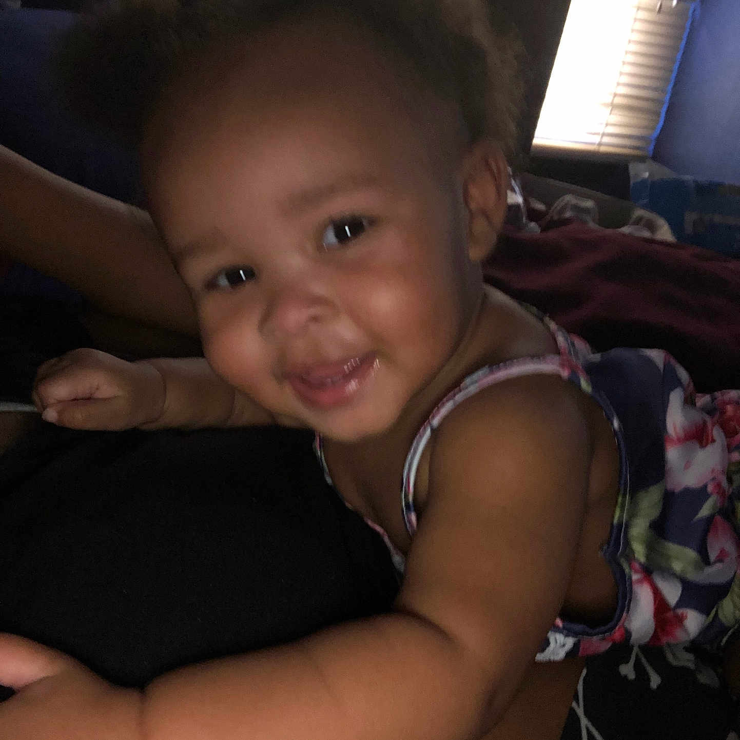 Kimani is registered to the contest to win money with this photo: baby, child, smile, face, hair, indoor, person, arm, clothing, floral_pattern, puffed_hair, expression, closeup, skin, shoulder, window_blinds, dark_background, cute, happy, infant