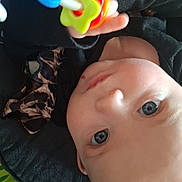 Alizah joined the competition — help win amazing prizes! baby, infant, rattle, toy, close_up, eyes, portrait, lying_down, play_mat, hand, colorful, indoor, clever_expression, skin, head, gaze, clothing, seat, blanket, newborn