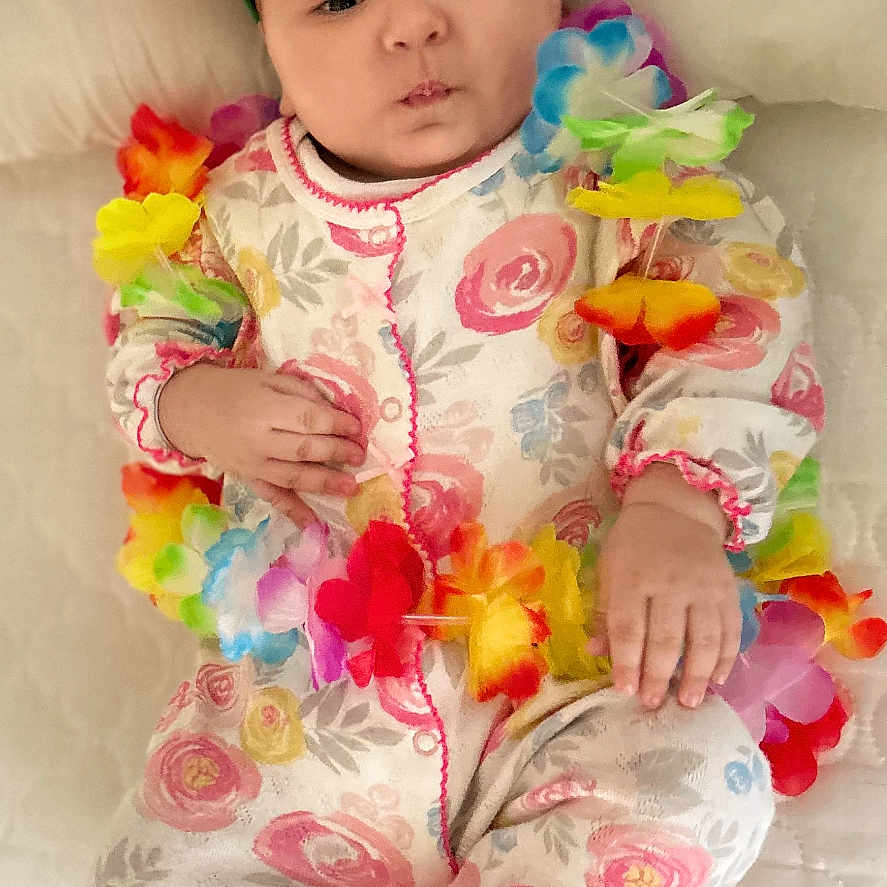 Shams is registered to the contest to win money with this photo: adorable, baby, baby_girl, blanket, colorful, cute, floral_onesie, flower_accessory, flower_crown, footie_pajamas, hand, indoors, infant, lei, lying_down, pajamas, portrait, puffed_cheeks, sleepwear, soft_lighting