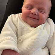 Luna participe au concours pour gagner de l'argent avec cette photo : baby, infant, smiling, closed_eyes, white_sweater, knitwear, hand, face, person, cute, newborn, portrait, sitting, indoor, cozy, skin, expression, happy, lap, clothing