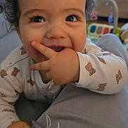 Wyatt participe au concours pour gagner de l'argent avec cette photo : baby, child, curly_hair, onesie, teddy_bear_pattern, hand, fingers, smile, happy, indoor, living_room, television, couch, person, closeup, cute, playful, infant, face, eyes