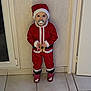 Juliette participe au concours pour gagner de l'argent avec cette photo : child, toddler, santa_claus_costume, red_clothing, pacifier, indoor, tile_floor, wall, door, window, slippers, pink_slippers, holiday, christmas, cute, baby, person, standing, clothing, face