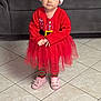 child, toddler, red_clothing, santa_hat, tutu, striped_leggings, pink_slippers, bunny_slippers, indoor, tiled_floor, sofa, holiday, festive, cute, portrait, person, young_child, floor, expression, costume