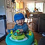 baby, blue_hat, chair, child, couch, daylight, dining_table, footwear, furniture, happy, home, indoor, kitchen, living_room, person, playtime, smiling, toy, walker, wooden_floor