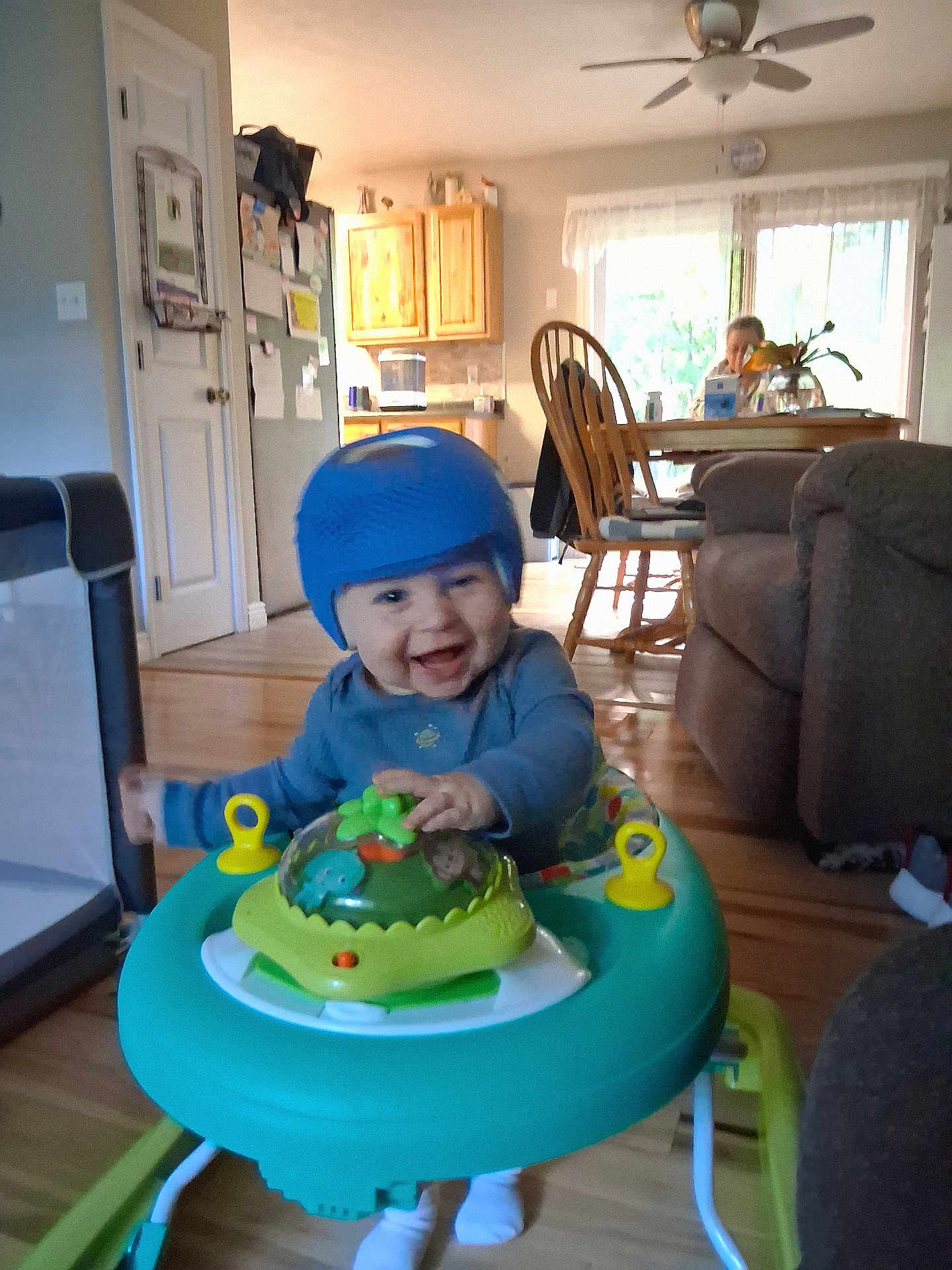 Onyx is registered to the contest to win money with this photo: baby, blue_hat, chair, child, couch, daylight, dining_table, footwear, furniture, happy, home, indoor, kitchen, living_room, person, playtime, smiling, toy, walker, wooden_floor