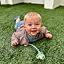 baby, infant, grass, pacifier, cardigan, blue_eyes, smile, happy, child, outdoor, toy, lying_down, cute, young_child, portrait, blond_hair, clothing, person, nature, daylight