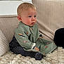 toddler, child, baby, striped_clothing, bib, green_bib, cartoon_animals, couch, cushions, plush_rug, indoor, portrait, sitting, curious, blue_eyes, blond_hair, soft_lighting, cozy, home, person