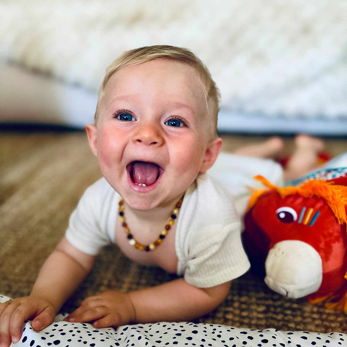 Mael participe au concours pour gagner de l'argent avec cette photo : amber_necklace, baby, blue_eyes, bright_eyes, carpet, cheerful, child, closeup, crawling, cute, happy, indoor, infant, orange_mane, playful, plush_toy, portrait, smiling, toy_horse, white_shirt