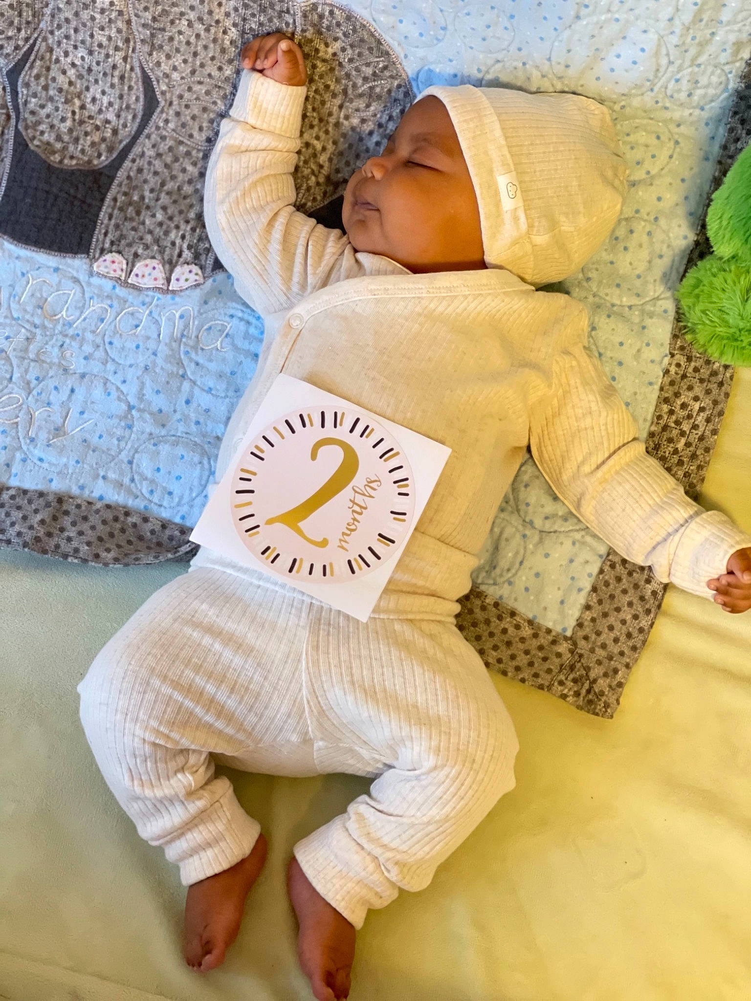 Amani is registered to the contest to win money with this photo: abdomen, baby_sleeping, bag, comfort, floor, flooring, happy, hat, headwear, human_leg, joint, knee, leisure, linens, pattern, person, sitting, sportswear, textile, thigh