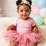 baby, toddler, pink_tutu, headband, curly_hair, smiling, sitting, blanket, knit_blanket, pastel_balloons, shoes, indoor, portrait, cute, child, happy, flower_headband, soft_lighting, decor, celebration