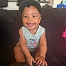 baby, toddler, smiling, cap, sleeveless_shirt, indoor, couch, child, happy, person, furniture, kitchen, household, seated, cute, portrait, young_child, bright, expression, casual