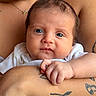 baby, infant, closeup, portrait, person, skin, tattoo, arm, hand, expression, face, newborn, clothing, white_shirt, holding, caring, adult, human, skin_tone, natural_light
