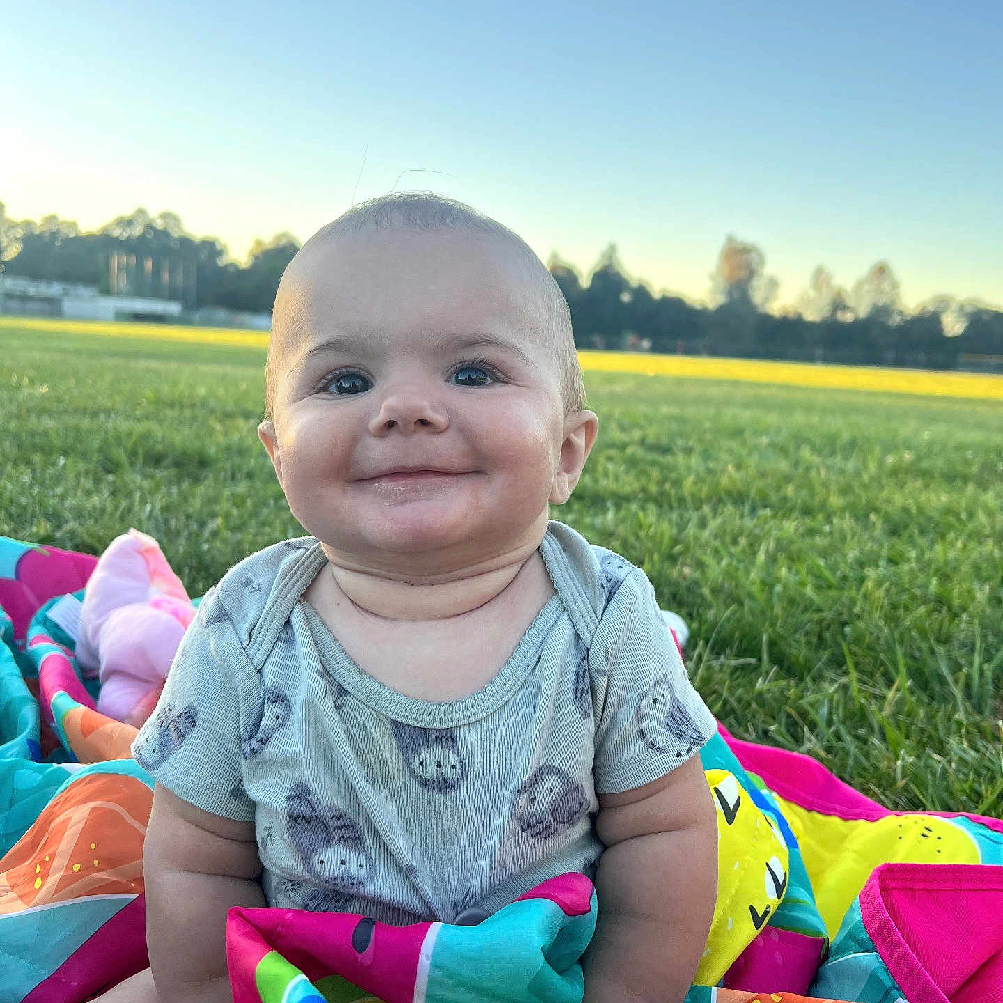 Lillian is registered to the contest to win money with this photo: baby, smiling, outdoor, grass, blanket, onesie, child, happy, cute, nature, sunset, field, colorful, infant, portrait, sky, sitting, face, person, playtime